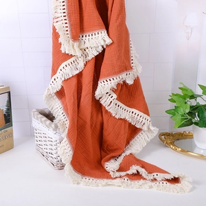 Detail of caramel muslin baby blanket featuring delicate lace tassels and crinkle texture