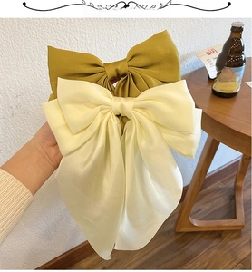Detail of oversized satin bow hair clips in mustard yellow and cream white finish
