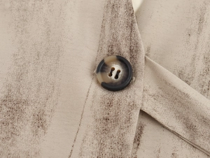 Dettaglio macro di un bottone nero e marrone su tessuto beige maculato del gilet