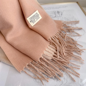 Close-up of pink imitation cashmere scarf texture featuring soft tassels and brand label