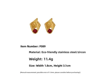 Detail view of gold conch shell earrings with red square zircon and steel texture