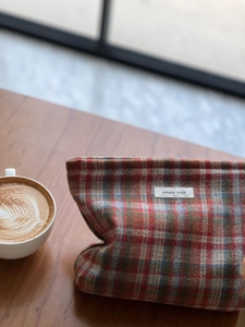 Detail of plaid tweed cosmetic bag with Simple Wish label on a cozy wooden desk