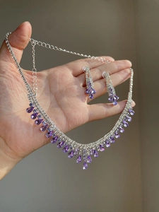 Detail of silver necklace and earrings set featuring purple teardrop crystals and studs