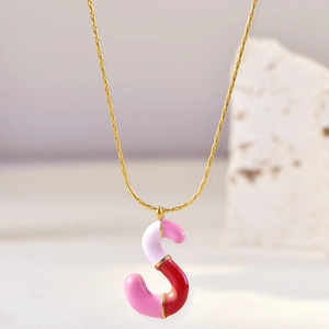 Macro shot of gold S-letter pendant with pink and red enamel on a stone surface