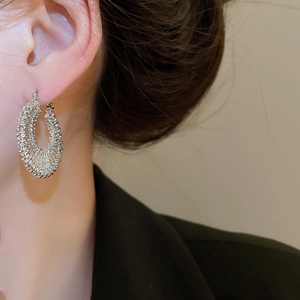 Close-up of silver braided texture hoop earring worn by a model in black attire