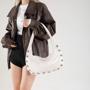 Chic white patent leather tote bag with silver studs worn by a model in casual attire