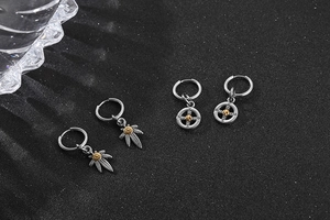 Macro shot of stainless steel hoop earrings with maple leaf and wheel rudder pendants