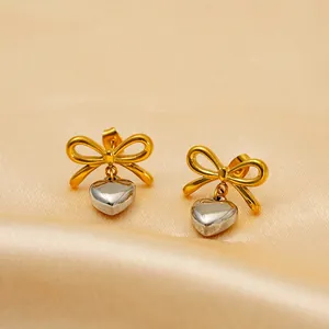 Chic gold bow and silver heart drop earrings on a champagne silk fabric background