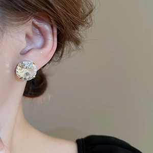 Close-up of a gold-plated stud earring with a large round claw-set crystal on model