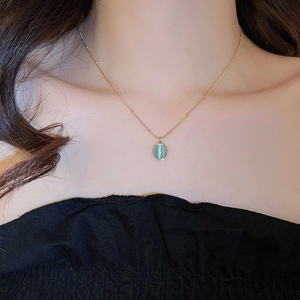 Elegant gold ball chain necklace featuring a green oval opal pendant on a model's neck