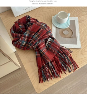 Detail of red plaid winter scarf with fringe on wood background with coffee cup