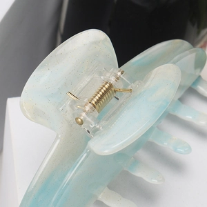Macro detail of gradient blue acrylic hair claw clip with golden glitter and durable spring