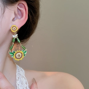 Detail of sunflower drop earrings with yellow enamel and green leaf accents on a model