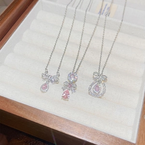 Detail of silver necklaces with pink teardrop pendants and bow accents in a jewelry box
