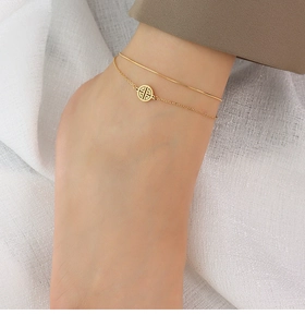 Detail of a double-layered 18k gold anklet with circular hollow pendant on model
