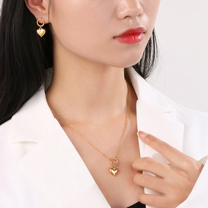 Elegant gold heart pendant necklace and earrings set worn by a model in a white suit