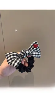 Detail of gingham bow hair scrunchie with red heart accent on a warm grey background