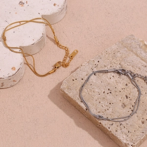 Detail of 18K gold and silver double-layered snake chain bracelets on stone background