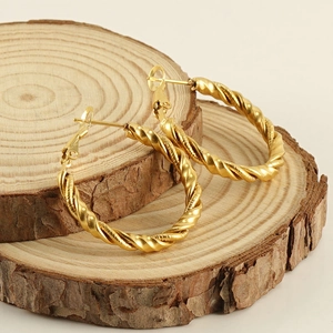 Detailed view of twisted gold hoop earrings with rope texture on a rustic wooden base