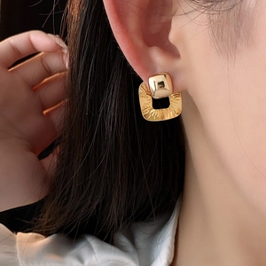 Macro view of gold plated square earrings with textured finish worn by a model
