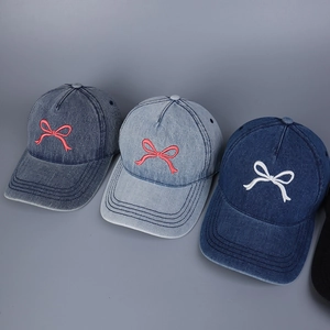 Detail der Stickerei mit rosa und weißen Schleifen auf blauen Denim-Baseballkappen