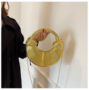 Detail einer metallisch goldenen Falten-Clutch mit rundem Griff und Kettenriemen
