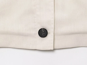 Détail de l'ourlet d'une veste beige en mélange de lin avec bouton noir et texture du tissu