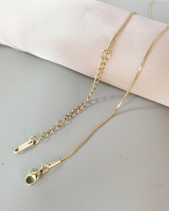 Detail of gold snake chain necklace with lobster clasp on pink silk roll and gray surface