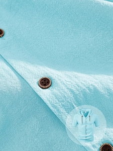 Macro detail of light blue linen hoodie shirt showing fabric texture and round buttons