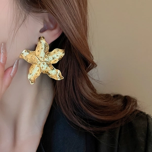 Macro detail of oversized gold starfish earrings with textured metallic finish on model