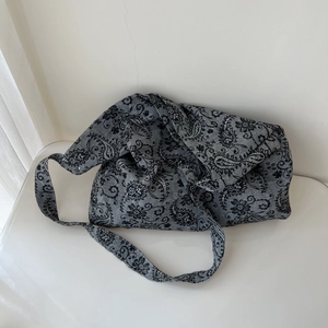 Detail of gray canvas crossbody bag featuring paisley patterns and a wide shoulder strap
