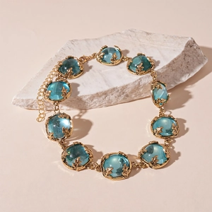Detail of gold chain necklace featuring translucent blue resin gems on white stone