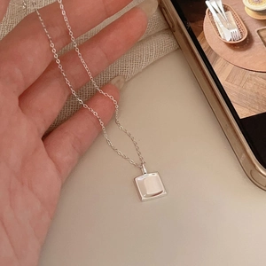 Close-up of minimalist square pendant necklace in silver finish on soft knit fabric