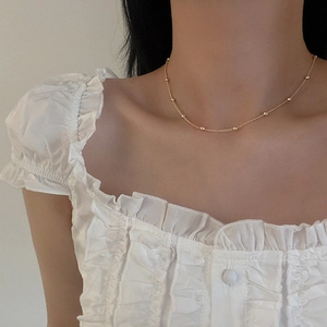 Dettaglio di una collana a catena minimalista con perline dorate indossata sulla clavicola