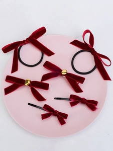 Detail of red velvet bow hair clips and black elastics on a pink round display plate