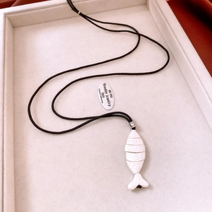 Close-up of white carved fish pendant on black cord necklace with silver beads