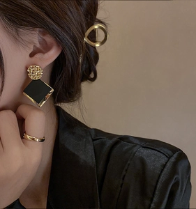 Detail shot of a model wearing geometric gold and black rhomboid earrings on a warm background