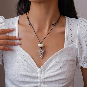 Detail of wax rope necklace with resin ring and silver grape bead pendant on model