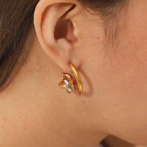 Close-up of mixed gold and silver twisted knot earrings worn on a model ear