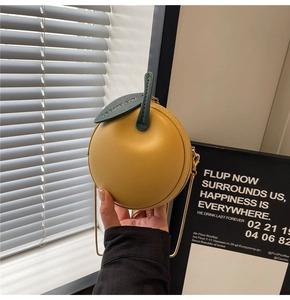 Detail of yellow apple-shaped leather crossbody bag with green leaf and chain strap