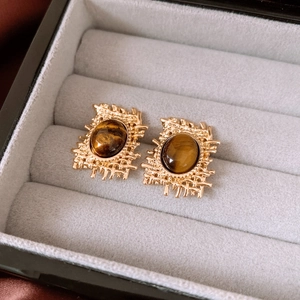 Close-up of vintage gold hollow earrings with oval tiger eye stone in a gray velvet box