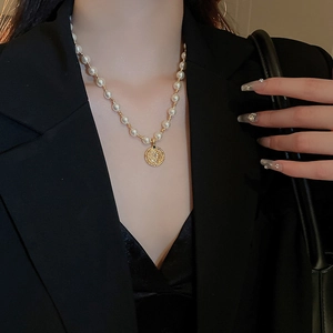 Nahaufnahme der Perlenkette mit goldenem Porträt-Münzanhänger auf schwarzem Blazer