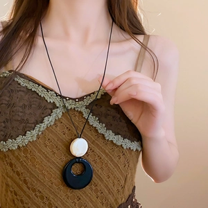 Détail d'un collier à pompon vintage avec texture marbrée et pendentif rond noir
