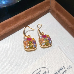 Detail of square gold-plated earrings with colorful zircon stones on woven texture