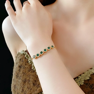 Detail of gold zircon bracelet featuring green square stones and adjustable pull chain