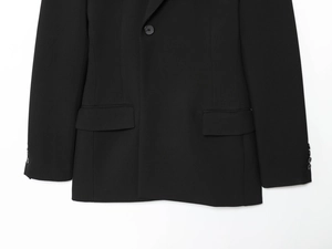 Gros plan sur la texture du blazer noir avec détails de bouton et poche à rabat