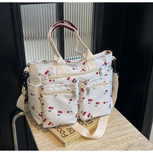 Close-up of white canvas tote bag with red cherry print and functional multi-pocket design