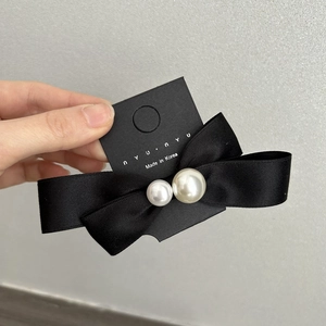 Detail of a black satin bow hair clip with decorative pearls on branded paper backing