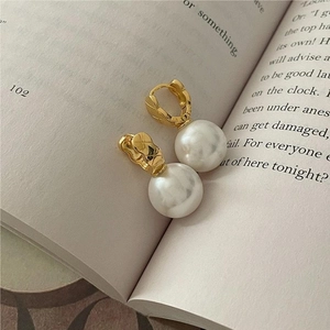 Macro shot of gold quilted hoop earrings with white pearls on a vintage book