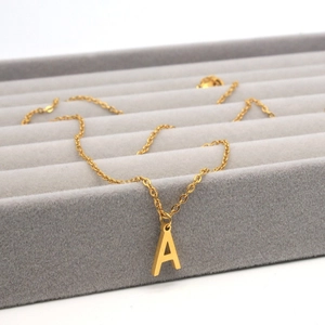 Macro shot of gold letter A pendant necklace on a luxury grey velvet jewelry tray